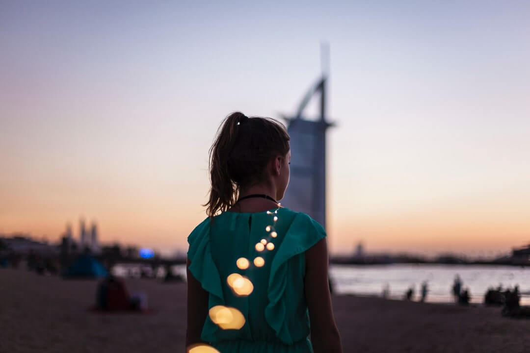 Donna di spalle davanti al Burj al-Arab la sera, si chiederà cosa vedere e cosa fare a Dubai.