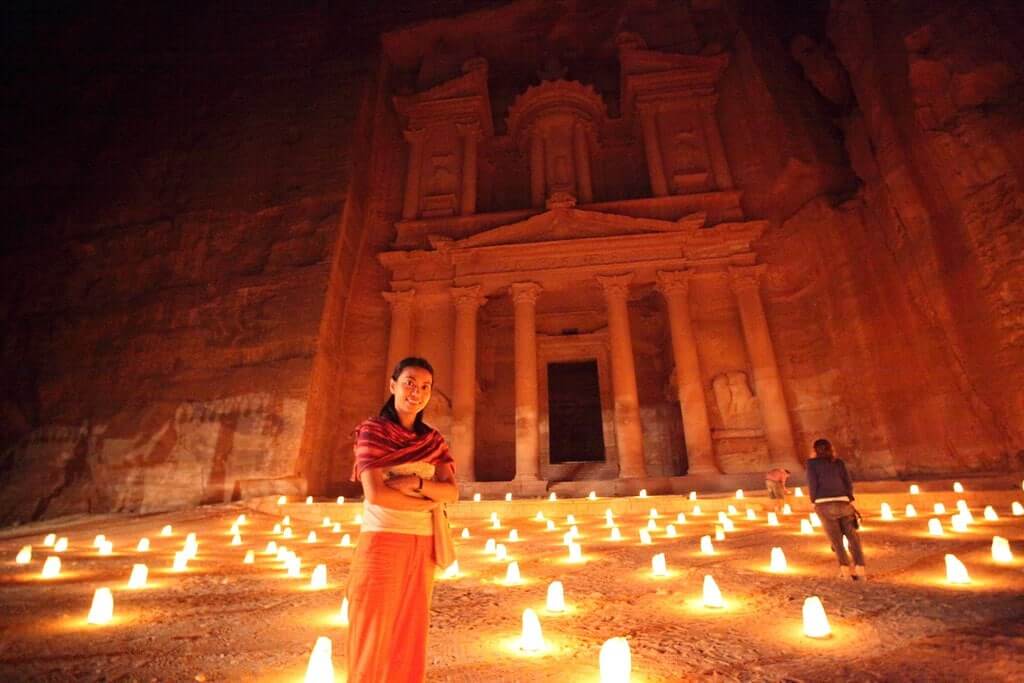 Donna sorridente davanti al Tesoro illuminato da candele luminose per il Petra by Night.