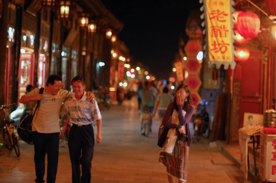 Alcune persone passeggiano alla luce delle lanterne rosse di Pingyao accese alla sera.