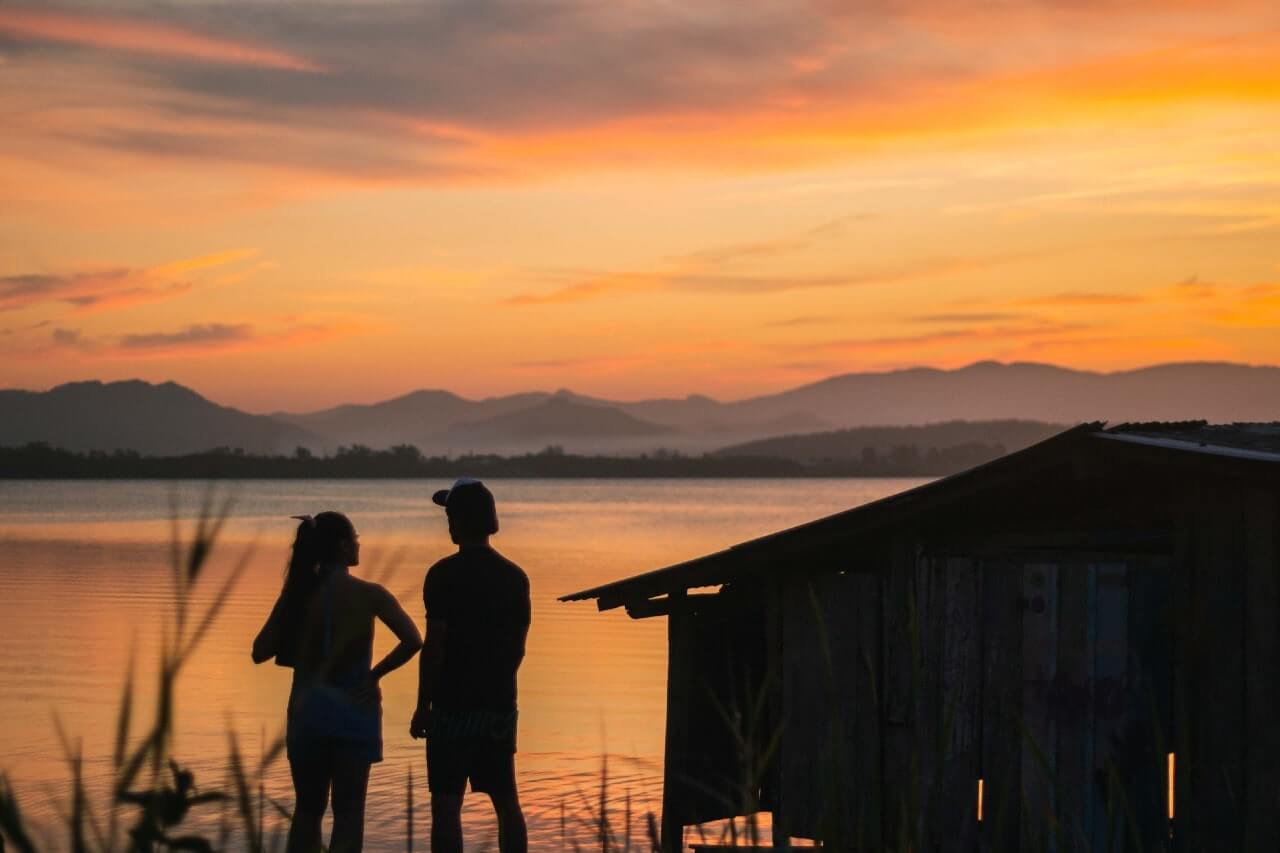 Due turisti ammirano il tramonto di fronte al mare alla Praia do Rosa di Imbituba, Brasile.
