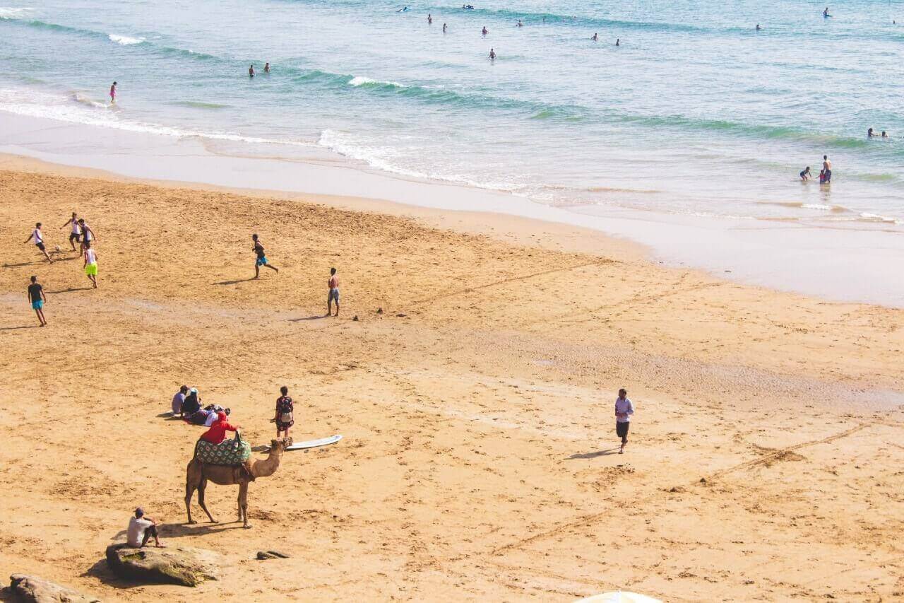 Bagnanti e un dromedario sulla spiaggia di Taghazout, in Marocco.