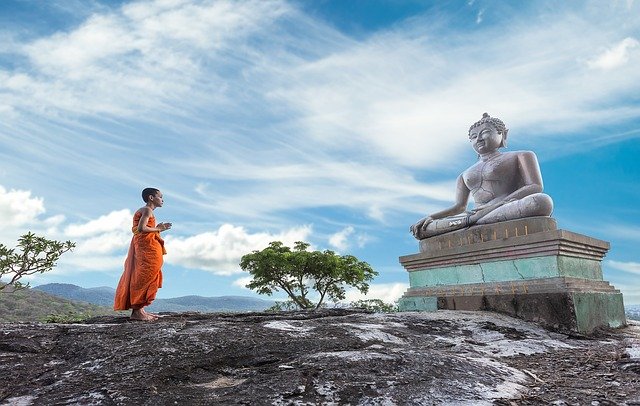 Un monaco buddhista in preghiera davanti ad una statua del Buddha. Goditi il tuo viaggio in Thailandia coi consigli di Amerigo.it