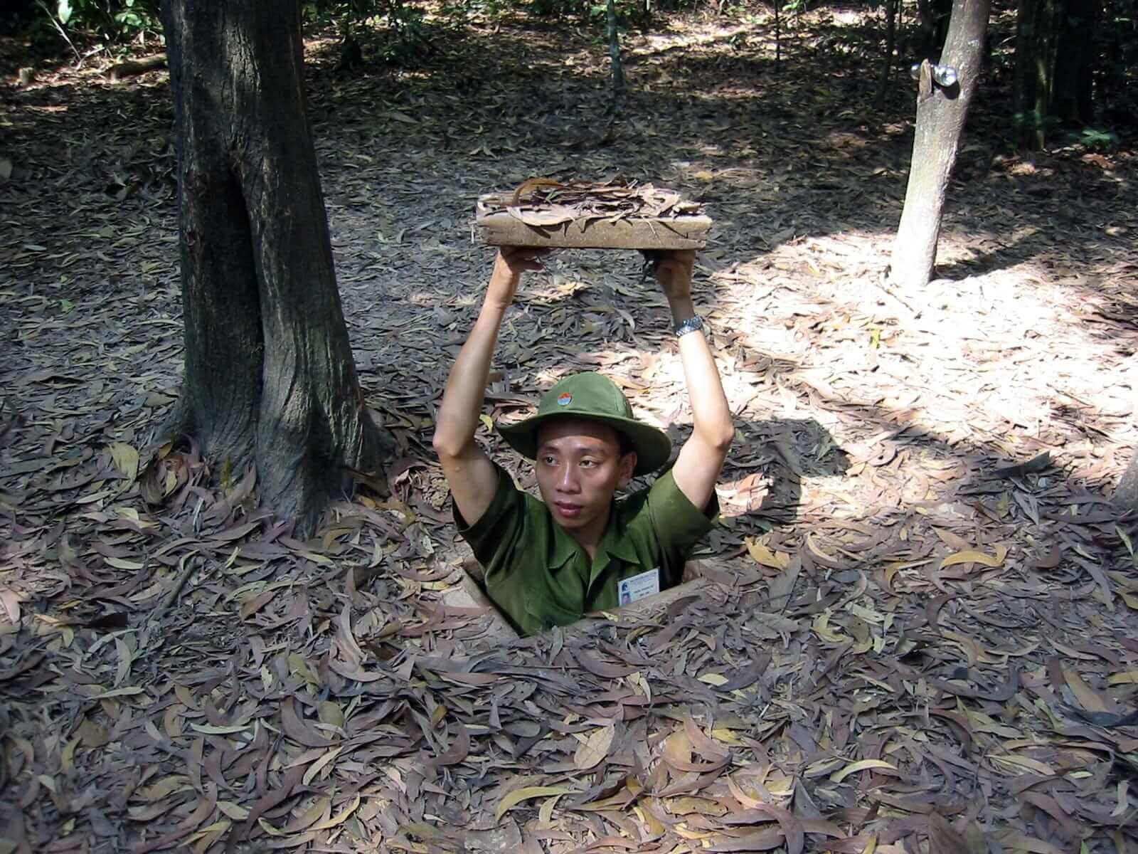 Uomo vietnamita che esce da una botola nascosta nel terreno comunicante con i Tunnel di Cu Chi.